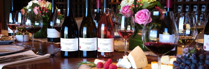 Three wine bottles on a set table with glasses of wine.