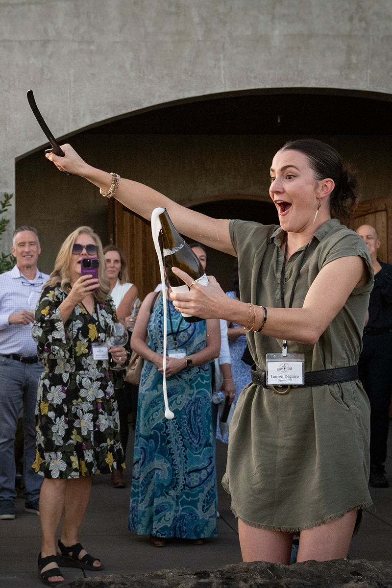 Woman sabering a bottle of sparkling wine.
