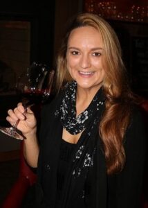 a woman holds a glass full of wine as she smiles.